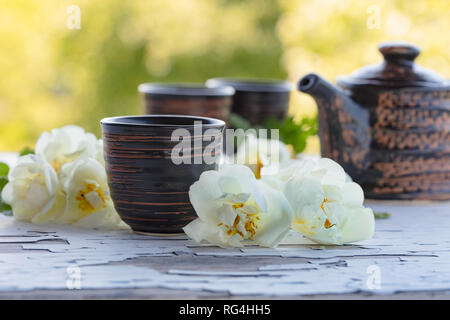 Keramik Tassen, Teekanne und weißen Hund Rosen an einem alten Holztisch in Garten. Aromatische und belebende Tee mit Wild Rose. Stockfoto