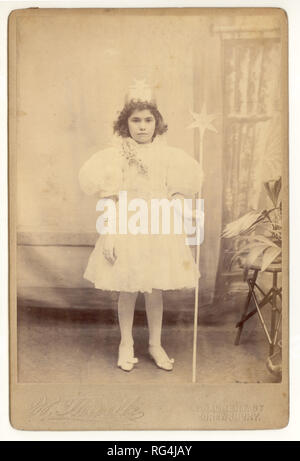 Original leicht verblasst, aber charmant viktorianischen Kabinettkarte Studio-Porträt von jungen Mädchen in weißen Feenkleid oder Königskleid mit einem Zauberstab, trägt eine Krone, für eine Party gekleidet. Fotografiert im W. Hewitts Studio, Shrewsbury, Shropshire, Großbritannien um 1895,1896. Stockfoto