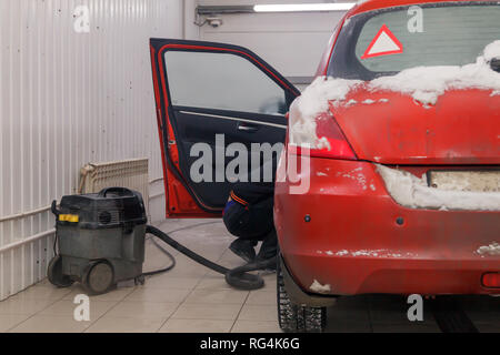 Russland Kemerovo 2019-01-05 Autowasherman sauber Suzuki Swift hellen roten Kleinwagen im Schmutz Schnee mit Staubsauger, professionelle chemische Reinigungsmittel. Co Stockfoto