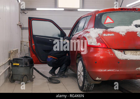 Russland Kemerovo 2019-01-05 Autowasherman sauber Suzuki Swift hellen roten Kleinwagen im Schmutz Schnee mit Staubsauger, professionelle chemische Reinigungsmittel. Co Stockfoto