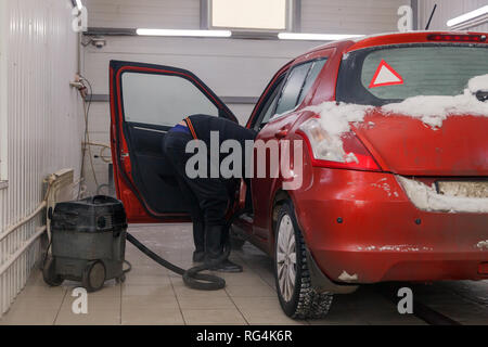 Russland Kemerovo 2019-01-05 Autowasherman sauber Suzuki Swift hellen roten Kleinwagen im Schmutz Schnee mit Staubsauger, professionelle chemische Reinigungsmittel. Co Stockfoto