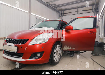 Russland Kemerovo 2019-01-05 Autowasherman sauber Suzuki Swift hellen roten Kleinwagen im Schmutz Schnee mit Staubsauger, professionelle chemische Reinigungsmittel. Co Stockfoto