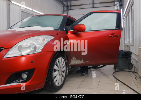 Russland Kemerovo 2019-01-05 Autowasherman sauber Suzuki Swift hellen roten Kleinwagen im Schmutz Schnee mit Staubsauger, professionelle chemische Reinigungsmittel. Co Stockfoto