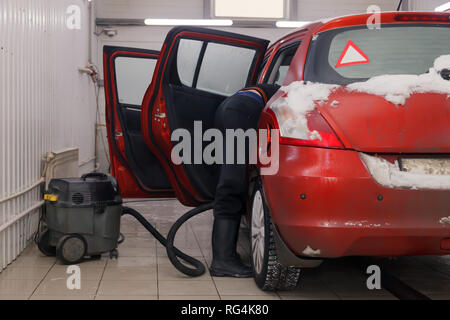 Russland Kemerovo 2019-01-05 Autowasherman sauber Suzuki Swift hellen roten Kleinwagen im Schmutz Schnee mit Staubsauger, professionelle chemische Reinigungsmittel. Co Stockfoto