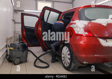 Russland Kemerovo 2019-01-05 Autowasherman sauber Suzuki Swift hellen roten Kleinwagen im Schmutz Schnee mit Staubsauger, professionelle chemische Reinigungsmittel. Co Stockfoto