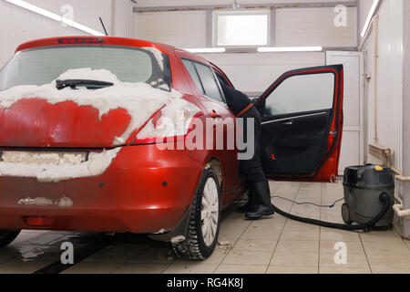 Russland Kemerovo 2019-01-05 Autowasherman sauber Suzuki Swift hellen roten Kleinwagen im Schmutz Schnee mit Staubsauger, professionelle chemische Reinigungsmittel. Co Stockfoto