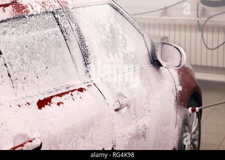 Autowasherman gilt weißer Schaum, professionelle chemische Reinigungsmittel für die Reinigung von Auto auf roten Kleinwagen. Konzept Reinigung Auto, bevor Sie das verkaufen, nach Schnee Stockfoto