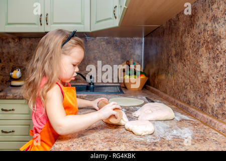 Wenig schöne süße Mädchen in orange Schürze lächelnd und hausgemachte Pizza, den Teig zu Hause Küche rollen. Konzept happy family Urlaub, Italia Stockfoto