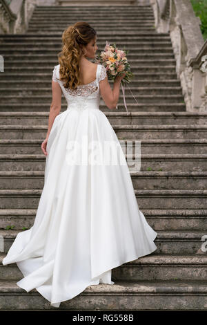 Anmutige Braut klettert die steinernen Treppen in einem Hochzeitskleid Stockfoto