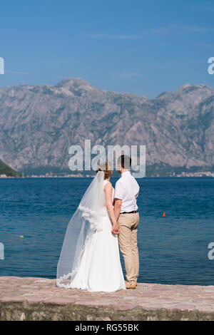 Brautpaar stand auf der Pier an einem sonnigen Tag und an das Meer, das Hände schauen Stockfoto