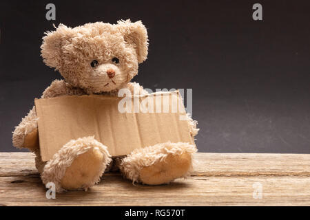 Armen obdachlosen Kind betteln. Teddy Bär traurig, mit einem leeren Karton Zeichen, sitzen in schwarzer Hintergrund, Kopie Raum Stockfoto