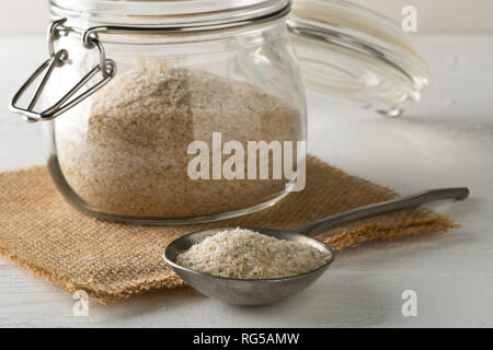 Haufen psyllium husk auch genannt Isabgol in Metall Löffel und Glas auf weißem Hintergrund. Psyllium husk auch genannt Isabgol ist Faser abgeleitet w Stockfoto