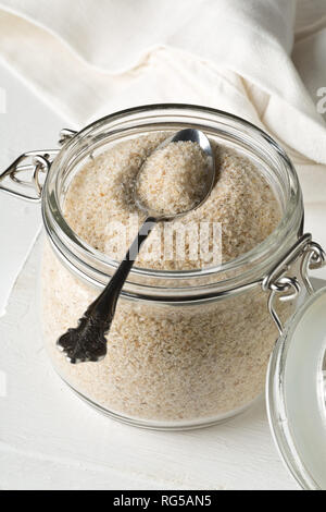 Haufen psyllium husk auch genannt Isabgol in Glas Glas mit metalllöffel auf weißem Hintergrund. Psyllium husk auch genannt Isabgol ist Faser abgeleitet Stockfoto
