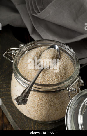 Haufen psyllium husk auch genannt Isabgol in Glas Glas mit metalllöffel auf dunklen Tisch Hintergrund. Psyllium husk auch genannt Isabgol ist Faser abgeleitet w Stockfoto
