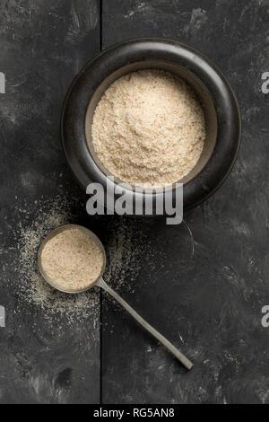 Haufen psyllium husk auch genannt Isabgol in Mörtel und Metalllöffel auf Schwarz tisch Hintergrund. Psyllium husk auch genannt Isabgol ist Faser abgeleitet von Stockfoto