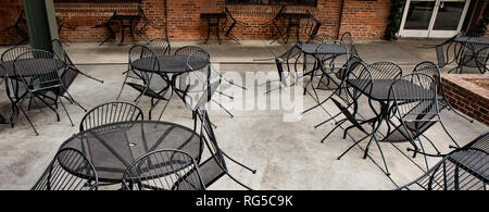 Geschlossener Sitzbereich im Freien einer städtischen Restaurant mit Bügeleisen Stühle gelehnt gegen Tabellen. Stockfoto