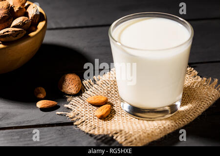 Bio ganze Mandeln Nüsse mit Schale in einem hölzernen Schüsseln und Mandelmilch auf schwarz Tabelle Stockfoto