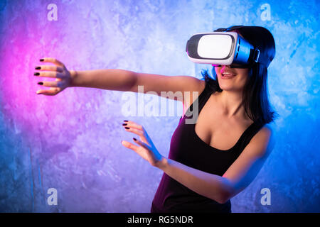 Schöne Pro-gamer Mädchen mit Virtual Reality Headset spielt im Online Video Spiel, gestikulierend. Coole Retro Neon Farben im Zimmer Stockfoto