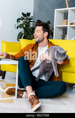Junge lachen Mann mit Laptop beim Sitzen auf dem Boden mit graue Katze Stockfoto