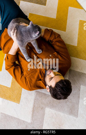 Blick von oben auf die gutaussehenden Mann liegen auf dem Teppich mit Britisch Kurzhaar Katze Stockfoto