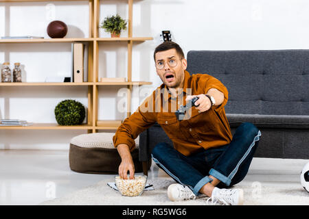 Schockiert man Fernsehen und sitzen in der Nähe der Schüssel mit Popcorn Stockfoto