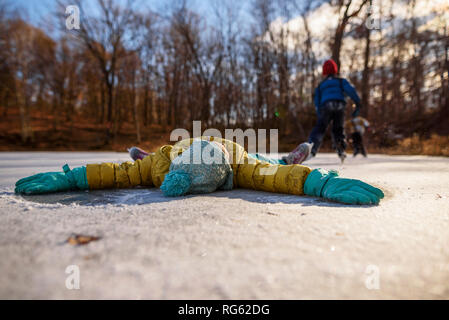 Mädchen liegt auf einem zugefrorenen Teich mit ihren ausgestreckten Armen und zwei Personen, Eislaufen im Hintergrund, United States Stockfoto