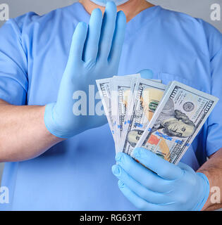 Arzt in der blauen Uniform und datex Handschuhe hält eine Menge Papier Geld und mit einer Geste der Hand zeigt Ablehnung Dollar Stockfoto