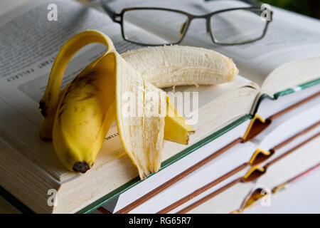 Bücher, Lesen Glas und halb gegessen Bananen Stockfoto