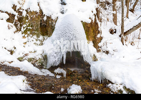 Ein kleiner Wasserfall in einem wilden Wald, ein Ice Dome mit eiszapfen Darüber gebildet, Schnee und ein wenig altes Gras Stockfoto