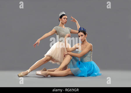 Zwei professionelle Ballerinas sitzen auf dem Boden im Studio und auf Kamera. Weibliche Ballett Tänzer tanzen und auf grauen Hintergrund isoliert. Konzept der Choreographie und Ballett. Stockfoto