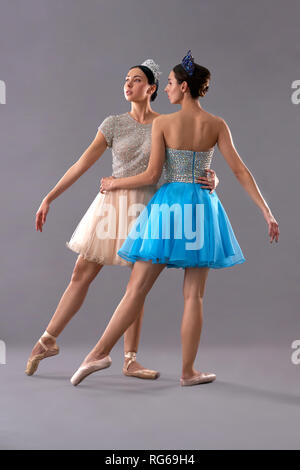 Zwei junge Tänzer zusammen auf grauem Hintergrund posiert. Schlanke Tänzerin in blauem Kleid stehen mit dem Rücken zur Kamera, während die weiblichen Partner voraus und beiseite stehen. Konzept des Balletts. Stockfoto