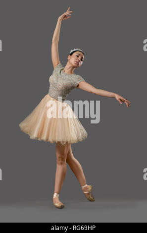 Schöne Ballerina in beige Kleid, Ballett Schuhe und Krone Tanz im Studio. Junge Künstler stehen auf Socken und posieren. Auf grauem Hintergrund. Begriff von Schönheit und Ballett Art. Stockfoto