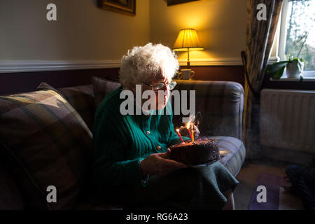 Ältere Frau ihren Geburtstag feiern mit Kuchen, während das Ausblasen der Kerzen, England, Vereinigtes Königreich Stockfoto
