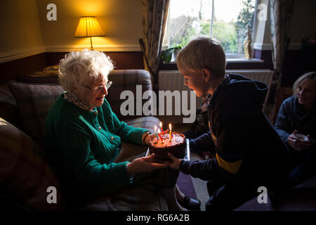 Ältere Frau und Enkel, die ihren Geburtstag mit einem Kuchen feiern, während sie die Kerzen ausblasen, England, Vereinigtes Königreich Stockfoto