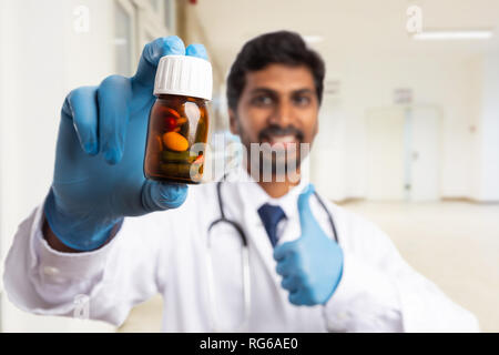 Close-up Flasche verordnungpillen von indischen männlichen Arzt oder Sanitäter lächelnd mit Daumen hoch, im Hintergrund gehalten Stockfoto
