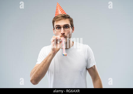 Studio geschossen von unrasiert Junge kaukasier männlich Blasen Pfeifen beim feiern Geburtstag, in entspannter und fröhlicher Ausdruck auf seinem Gesicht Stockfoto