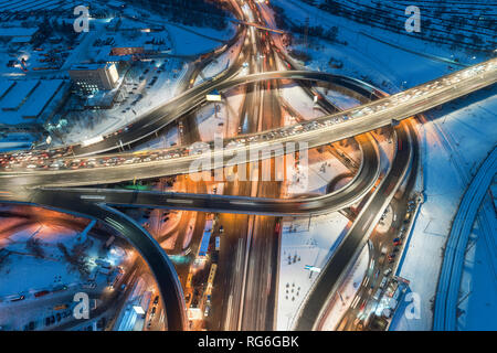 Luftaufnahme der Weg in die moderne Stadt in der Nacht im Winter. Blick von oben auf den Verkehr in Highway Kreuzung mit Beleuchtung. Erhöhte Straße und Interchange ov Stockfoto