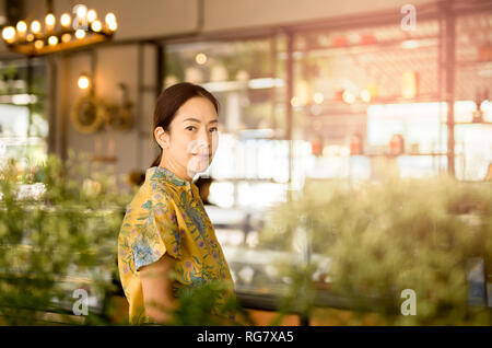 Schöne asiatische Frau mittleren Alters an der Kamera im Coffee Shop. Stockfoto