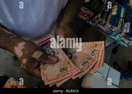 Caracas, Venezuela. 28 Jan, 2019. Ein Mann, der selbst gemachte Kopien von Filmen zählt Rechnungen nach einem Verkauf verkauft. Vom 28.01.2019, das private Geld Haus Interbanex Devisengeschäfte in der sozialistischen Land führen kann. Am ersten Handelstag, der Bank der Wechselkurs bei 3200 Bolivar pro Dollar. Dies bedeutete eine Abwertung von knapp 35 Prozent gegenüber dem offiziellen Wechselkurs der Zentralbank. Credit: Marcelo Perez del Carpio/dpa/Alamy leben Nachrichten Stockfoto