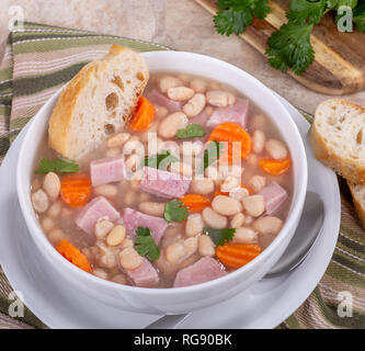 Ansicht von oben aus einer Schüssel Schinken und Bohnensuppe mit Karotten in Scheiben geschnitten und französischem Brot Stockfoto