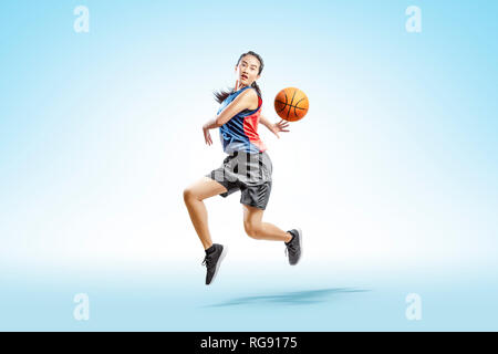 Attraktive asiatische Frau spielen Basketball über hellen Hintergrund Stockfoto