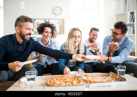 Gruppe von jungen männlichen und weiblichen Geschäftsleuten mit Pizza zu Mittag essen in einem modernen Büro. Stockfoto