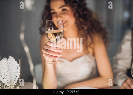 Eine Nahaufnahme einer jungen Braut an einem Tisch auf einer Hochzeit sitzend, mit einem Glas Weißwein. Stockfoto