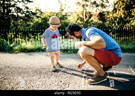 Vater Zeichnung Hopse auf Asphalt, während sein kleiner Sohn ihn beobachtete Stockfoto