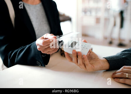 Ein Mittelteil der unkenntlich Kunde und Verkäufer das kontaktlose Bezahlen in einem Shop. Stockfoto