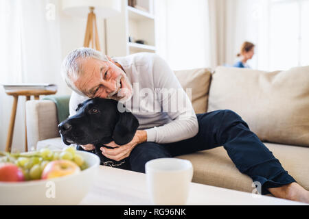 Ein älteres Paar im Innenbereich mit einem schwarzen Hund zu Hause, eine gute Zeit. Stockfoto