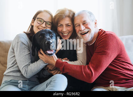 Ein älteres Paar mit ein junges Mädchen sitzt auf einem Sofa mit Hund zu Hause. Stockfoto