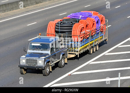 Aussicht auf Land Rover Defender & Trailer Transport der sortierten Color Coil & gerade flexible Kunststoffschlauch Schlauch de Autobahn entlang fahren Stockfoto