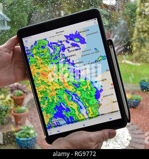 Frau Hände halten des ipad pro Tablette regen Alarm app nutzt Echtzeit Farbe radardaten überlagernden Niederschlag auf der lokalen Karte regnerische Wetter auf Fenster Essex UK Stockfoto