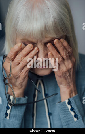 Portrait der älteren Frau mit Brille und graues Haar wischte sich und zu Hause weinen Stockfoto